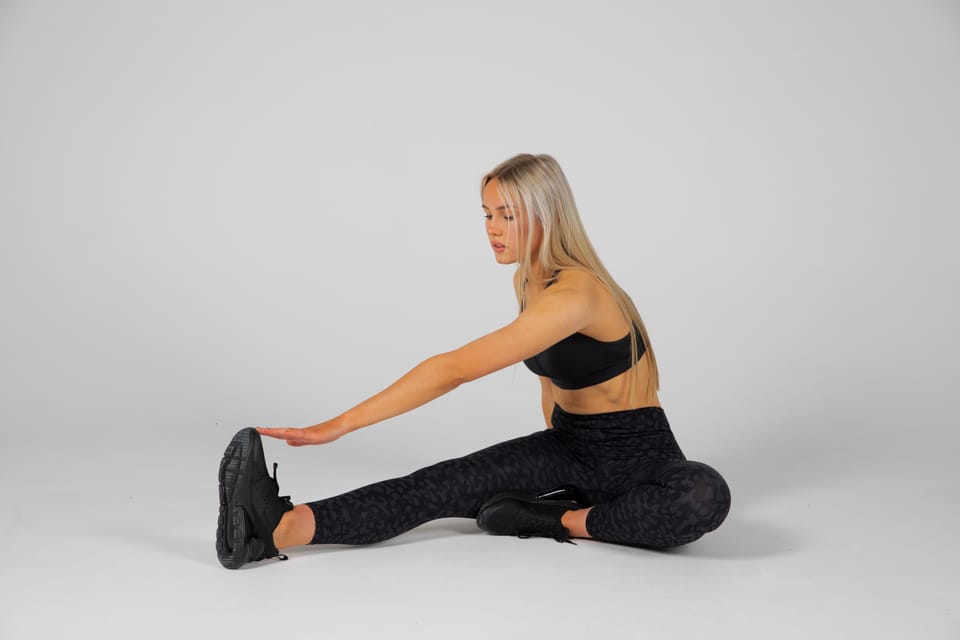 Maria in a seated hamstring stretch, reaching for her toes in the studio.
